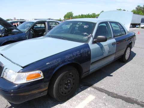 1991 Ford LTD Crown Victoria - A two-tone police car sits in a lot with its hood and trunk open, showing visible damage and writing on the fender.