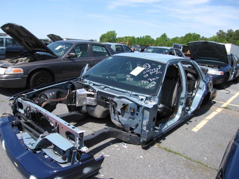 1991 Ford LTD Crown Victoria - Car chassis stripped of most parts, parked in a salvage yard with other vehicles.