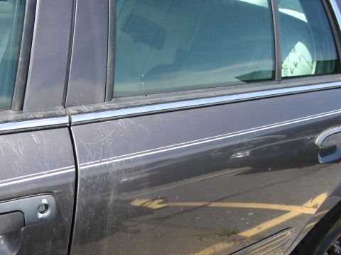 1991 Ford LTD Crown Victoria - Side view of a dark gray sedan, showing the door panel with chrome trim and numerous scratches.