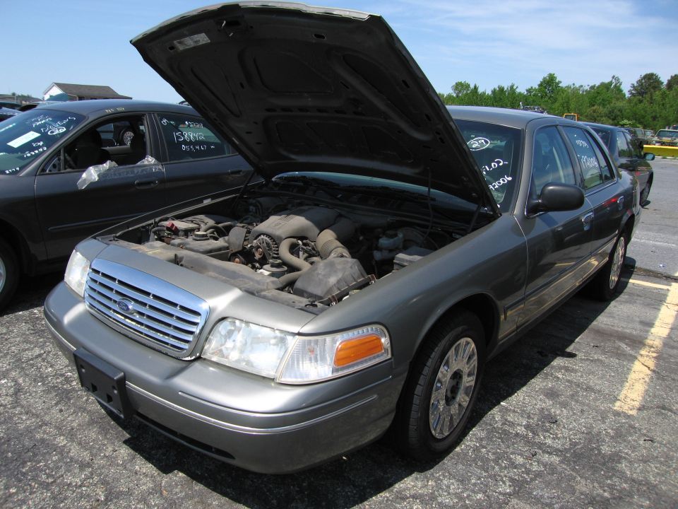 Gray Ford Crown Victoria with hood open, showing engine. Visible text on windshield and door