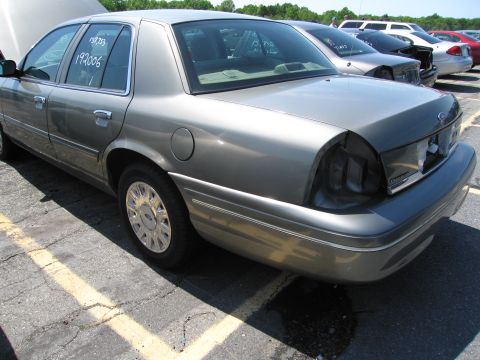 1991 Ford LTD Crown Victoria - A gray sedan is parked in a lot, showing damage to the rear with a missing taillight and text on the window.
