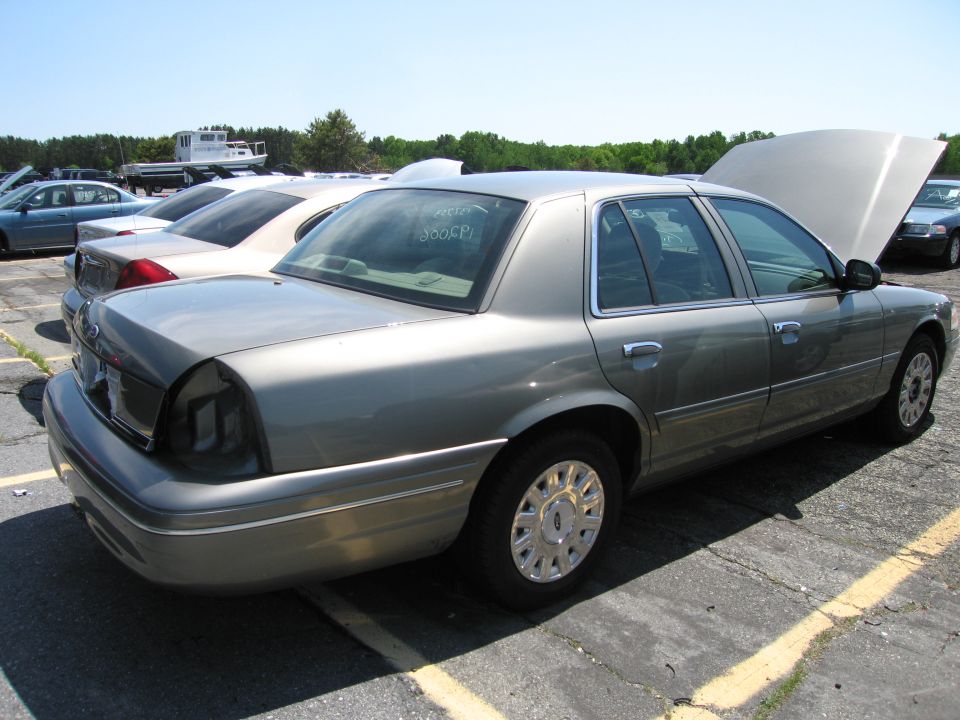 Gray Ford Crown Victoria parked in lot with hood open, other cars visible