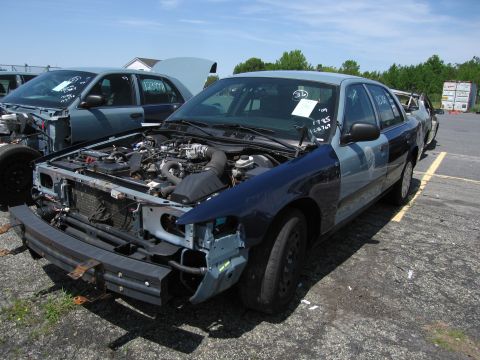 1991 Ford LTD Crown Victoria - A two-tone Ford Crown Victoria sits in a junkyard with its hood open, revealing the engine and a missing front bumper.