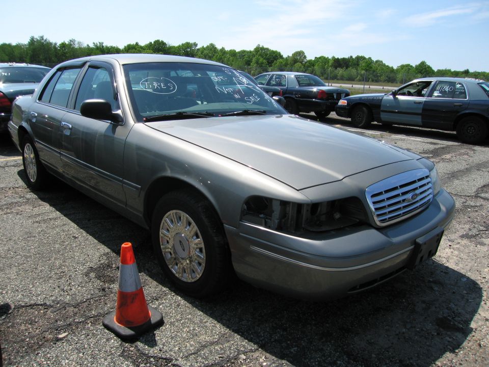 Gray Ford Crown Victoria with missing headlights, parked in a lot with other cars