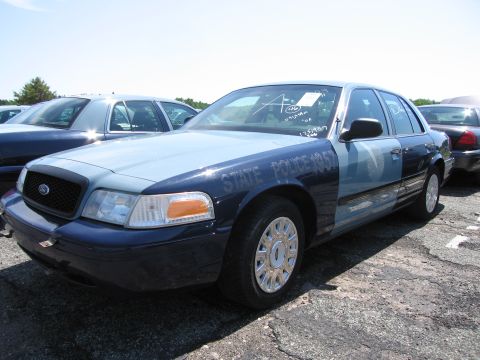 1991 Ford LTD Crown Victoria - A two-tone Ford Crown Victoria police car, marked "STATE POLICE 1957", is parked in a lot with other vehicles.
