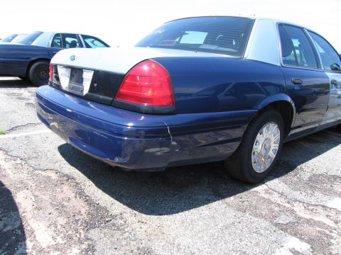 1991 Ford LTD Crown Victoria - Two blue and silver Ford Crown Victorias are parked outside on a lot. The foreground car shows damage to its rear bumper.