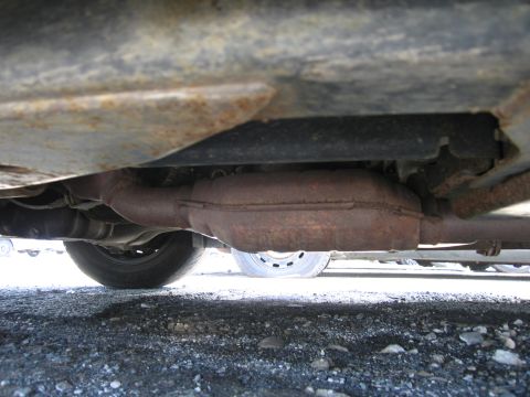 1991 Ford LTD Crown Victoria - Close-up of a vehicle's rusty exhaust system and undercarriage, with a tire visible.