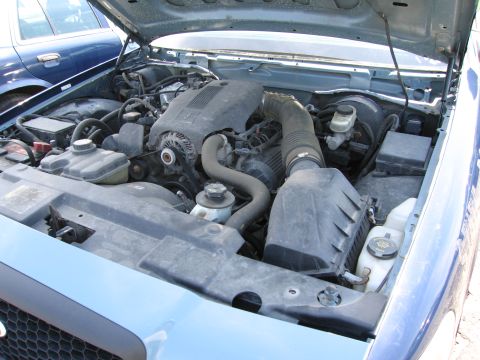 1991 Ford LTD Crown Victoria - The engine compartment of a blue sedan is shown, with another vehicle partially visible in the background.