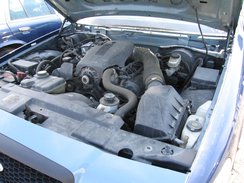 Engine bay of a blue car, another blue car visible behind it