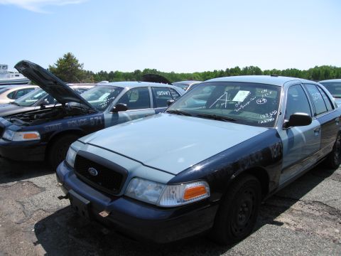 1991 Ford LTD Crown Victoria - Two police cruisers are parked in a lot, one with its hood open. The front vehicle is a light blue and black Ford Crown Victoria.