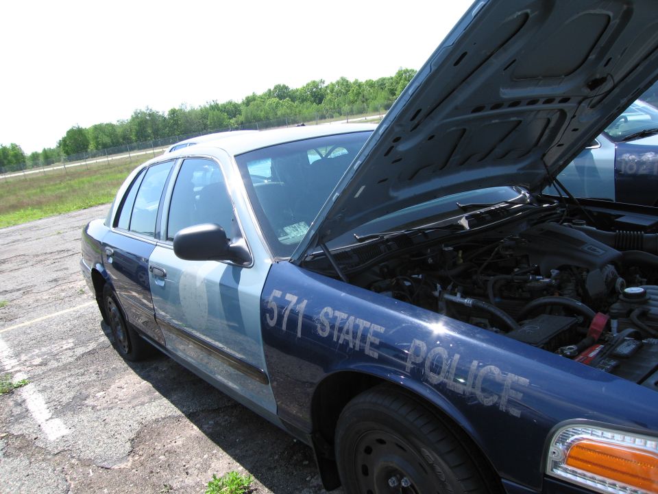 Blue and white police car with hood open, showing engine. "571 STATE POLICE" text visible