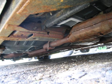1991 Ford LTD Crown Victoria - The underside of a car shows significant rust on the frame and exhaust components.