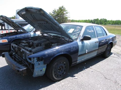 1991 Ford LTD Crown Victoria - Two police cars are parked outside with their hoods open. One has a missing bumper and mismatched paint on its doors.