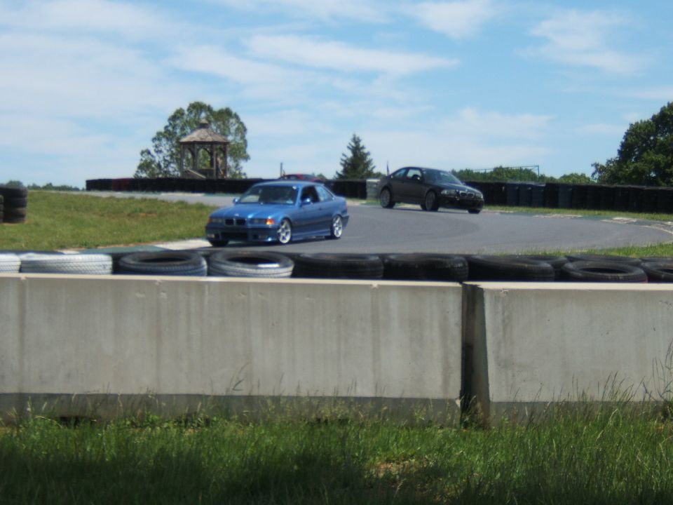 Blue BMW coupe and dark BMW sedan on a road-course track behind tire wall