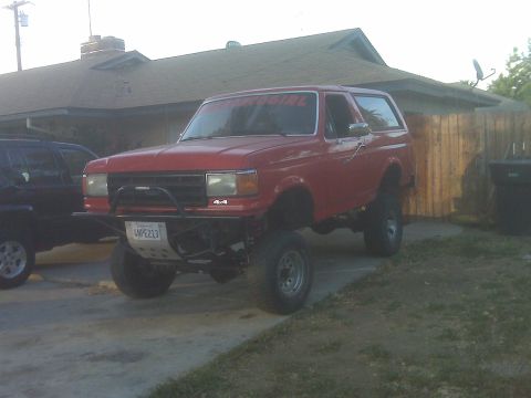 1969 Ford F-250 - This lifted red Ford Bronco has a "4x4" badge and a "SUPERGIRL" sticker on the windshield.