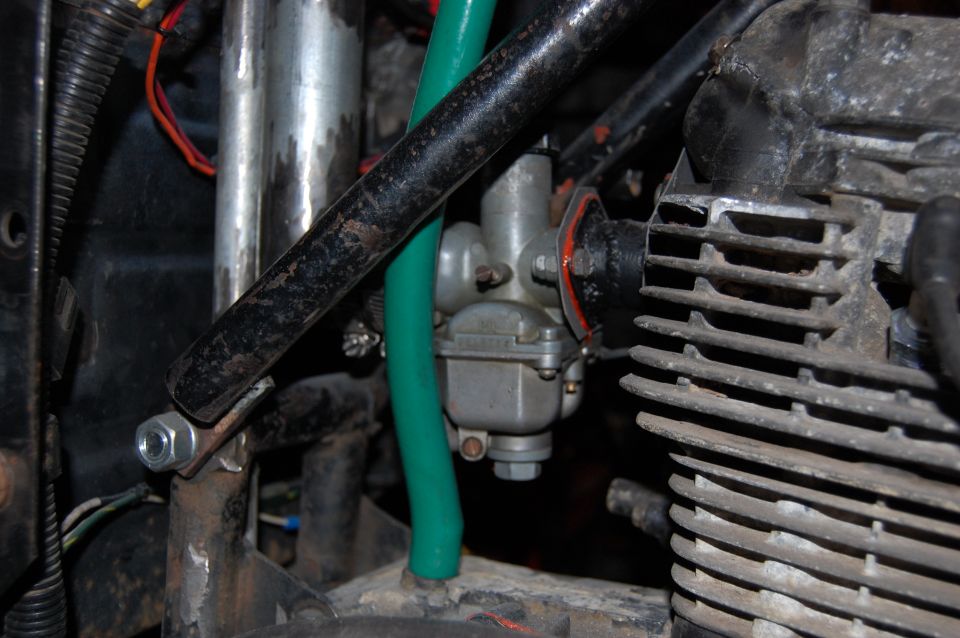 Close-up of a motorcycle's carburetor and part of the engine block. Green fuel line visible