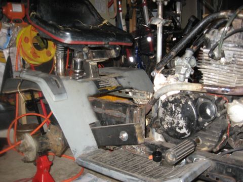 2010 Kawasaki BAYOU 220 - Close-up view of a motorcycle's engine and seat, showing mechanical components and workshop clutter.