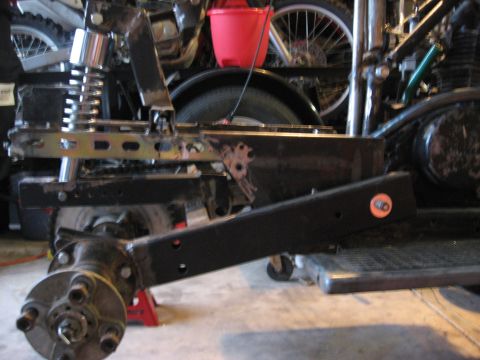 2010 Kawasaki BAYOU 220 - Close-up of an ATV's frame and suspension components, with a red bucket and bicycle wheels visible in the background.