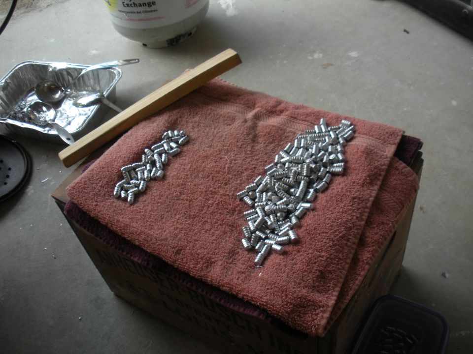 Two piles of small screws on a red towel, with a metal tray and wooden stick nearby