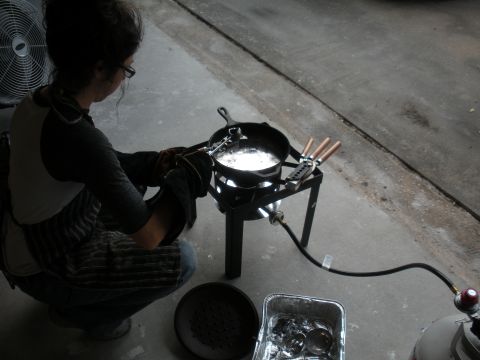 1996 Ford Bronco - A person wearing gloves and an apron crouches to cast metal over a propane burner, with a fan in the background.