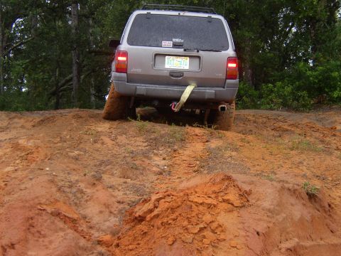 1991 Ford Bronco - A Jeep Grand Cherokee navigates a muddy off-road trail, its rear end angled upwards.