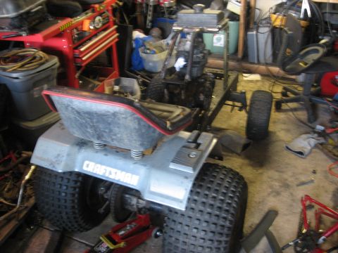 2010 Kawasaki BAYOU 220 - A Craftsman riding mower is shown in a cluttered garage, possibly undergoing repairs or maintenance.