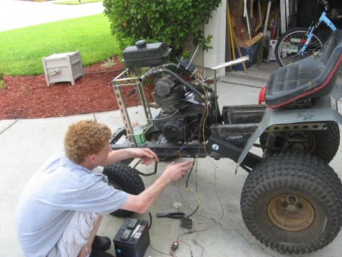 2010 Kawasaki BAYOU 220 - A person works on the wiring of a disassembled lawn tractor in a driveway.