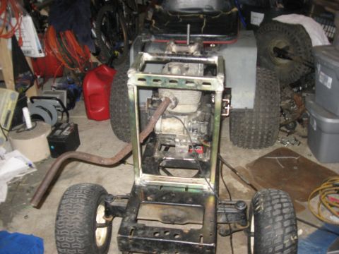 2010 Kawasaki BAYOU 220 - The chassis of a lawn tractor is shown in a cluttered garage setting, with its engine exposed.