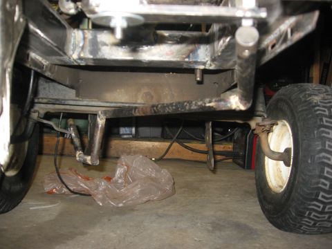 2010 Kawasaki BAYOU 220 - The underside of a lawn tractor shows its frame, suspension, and tires, with a plastic bag on the floor.