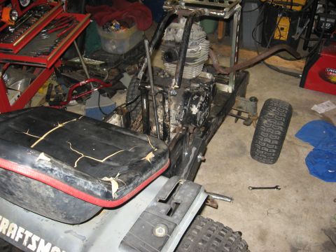 2010 Kawasaki BAYOU 220 - A Cushman lawn tractor is shown in a garage with a detached wheel and a cracked seat, surrounded by tools and equipment.