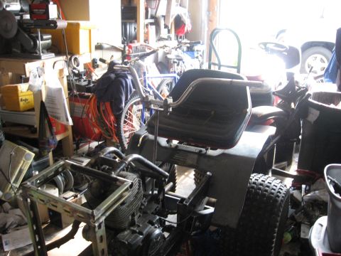 2010 Kawasaki BAYOU 220 - Lawn tractor in a garage, surrounded by tools, bicycles, and other items.