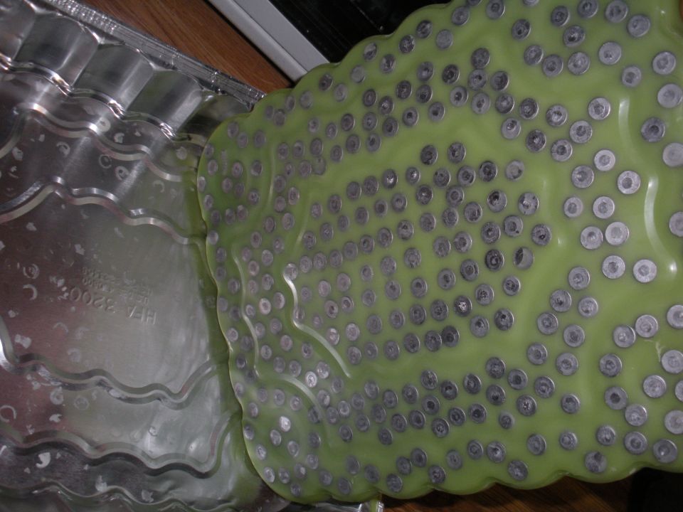 casting mold with many small metal inserts on a green surface next to a wavy metal sheet