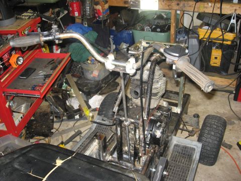 2010 Kawasaki BAYOU 220 - A three-wheeled vehicle with its engine and handlebars visible is shown in a cluttered garage setting.