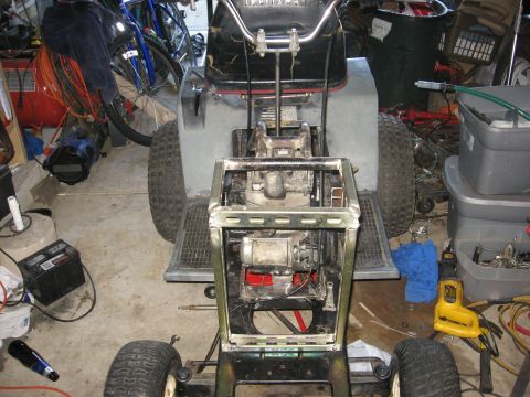 2010 Kawasaki BAYOU 220 - A lawn tractor is shown in a state of repair, with its engine and frame disassembled in a cluttered garage setting.