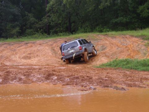 1991 Ford Bronco - A silver SUV struggles in deep mud, with a person attempting to push it free.