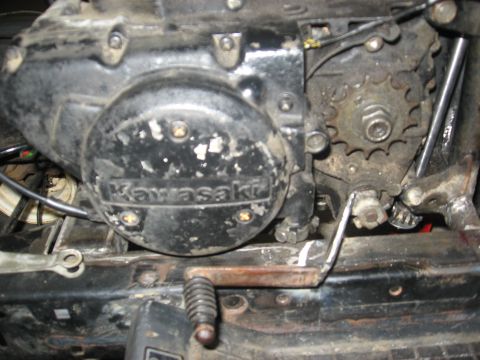 2010 Kawasaki BAYOU 220 - Close-up view of a Kawasaki engine, showing the casing, chain sprocket, and shifter mechanism.