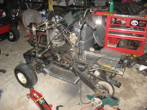 2010 Kawasaki BAYOU 220 - A custom-built go-kart frame is shown in a cluttered garage setting with various tools and equipment around it.
