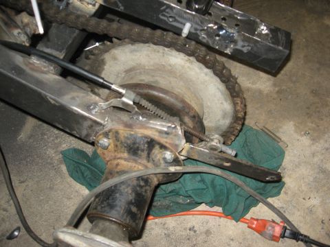 2010 Kawasaki BAYOU 220 - Close-up view of a motorcycle's rear axle, chain, and brake assembly.