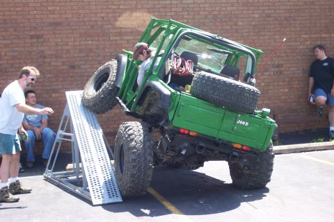 1992 Ford Bronco - A modified green Jeep is attempting to climb a ramp during an off-road event.