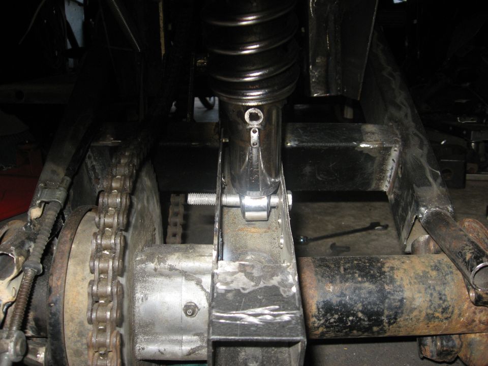 Close-up of ATV rear axle, chain, and shock absorber assembly. Some metal fabrication is visible