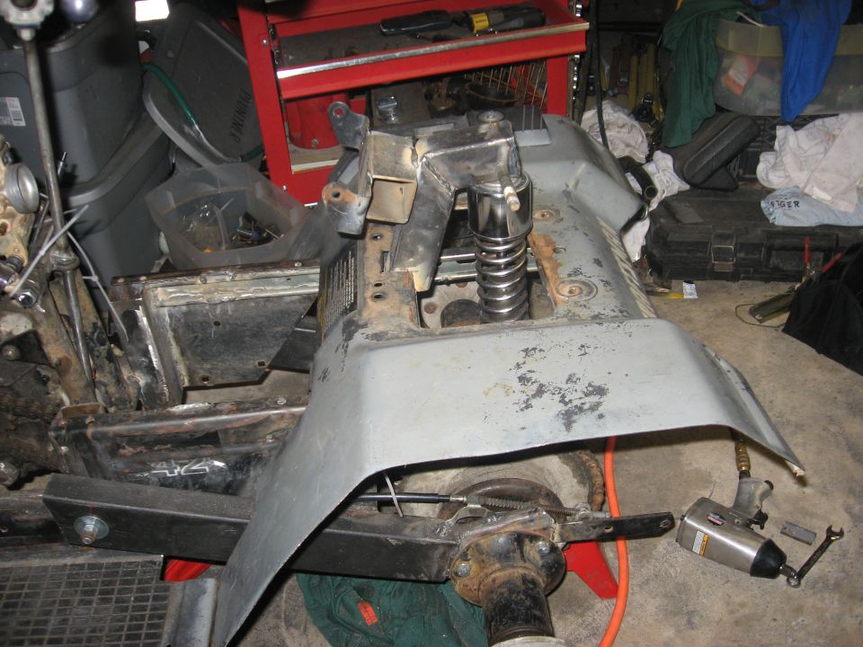 Disassembled ATV rear end in a garage with bare fender panel and exposed coil-over shock