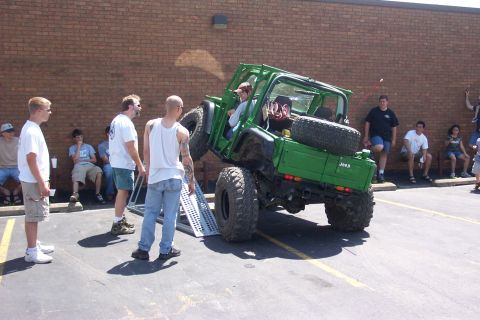 1992 Ford Bronco - A green Jeep Wrangler is being driven up a ramp by onlookers.