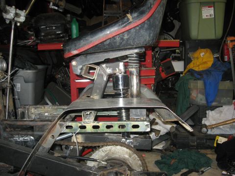 2010 Kawasaki BAYOU 220 - Close-up view of the seat and frame assembly of an ATV, with visible suspension components and chain drive mechanism.