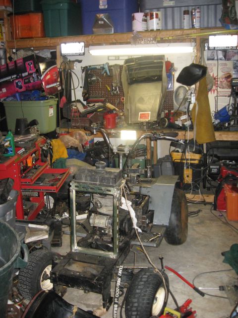 2010 Kawasaki BAYOU 220 - A lawn tractor is partially disassembled in a cluttered garage, with tools and storage bins visible in the background.