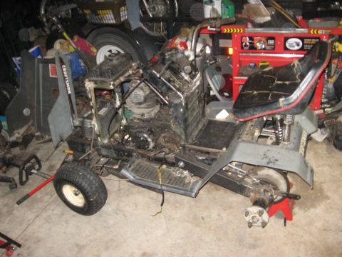 2010 Kawasaki BAYOU 220 - A disassembled lawn tractor sits in a cluttered garage, awaiting repairs.