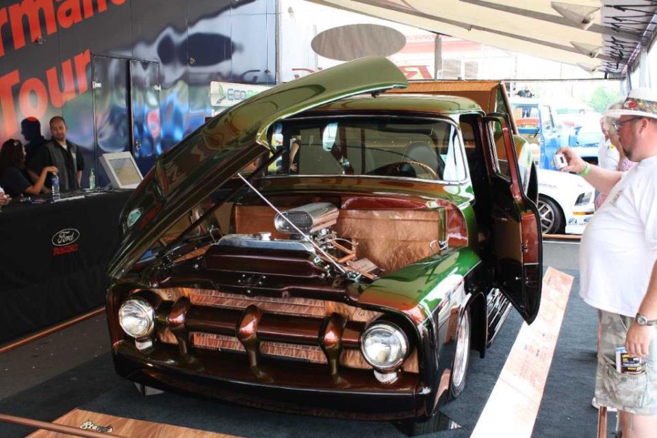 Green and brown Ford F-100 pickup truck with hood and door open, showing engine and interior