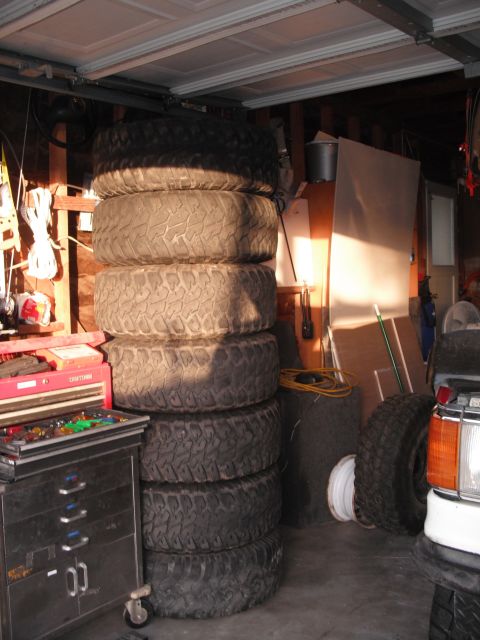 1991 Ford Bronco - A tall stack of off-road tires is stored in a garage next to a toolbox and a partial view of a vehicle.