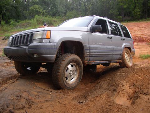 1991 Ford Bronco - A silver Jeep Grand Cherokee navigates a muddy incline during an off-road excursion.