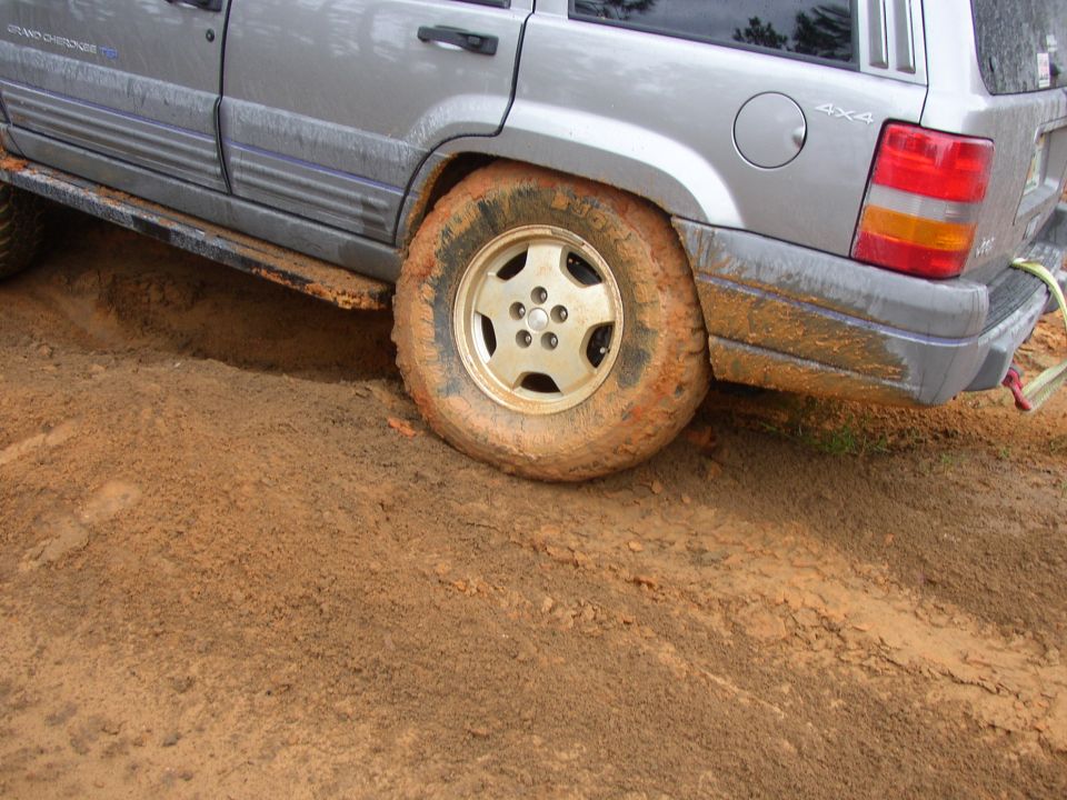 Silver Jeep Grand Cherokee with mud-covered tires stuck in dirt