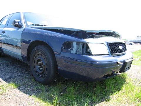 1991 Ford LTD Crown Victoria - A damaged blue Ford Crown Victoria sits in a grassy lot with its hood open and one headlight missing.
